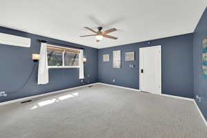 Empty room with a ceiling fan, carpet floors, baseboards, and a wall mounted AC