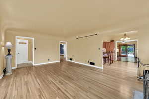 Unfurnished living room with baseboards, a notable chandelier, and light wood-type flooring