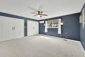 Unfurnished bedroom featuring carpet, a wall unit AC, multiple closets, visible vents, and baseboards