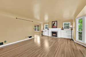 Unfurnished living room featuring a lit fireplace, a wealth of natural light, baseboards, and light wood-type flooring
