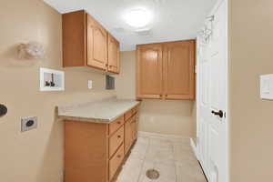 Clothes washing area with electric dryer hookup, cabinet space, a textured ceiling, visible vents, and baseboards