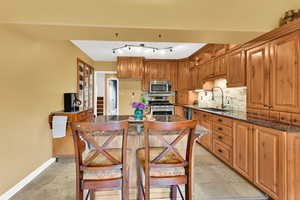 Kitchen featuring a sink, dark stone counters, baseboards, backsplash, and appliances with stainless steel finishes