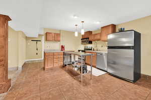 Kitchen with baseboards, light tile patterned floors, hanging light fixtures, light countertops, and appliances with stainless steel finishes