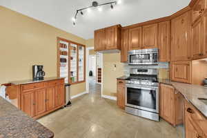 Kitchen featuring dark stone counters, appliances with stainless steel finishes, brown cabinetry, and baseboards