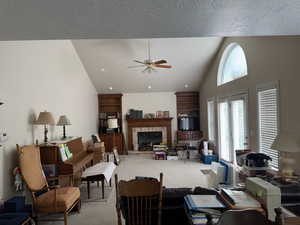 Living room featuring a ceiling fan, a textured ceiling, a brick fireplace, vaulted ceiling, and carpet floors