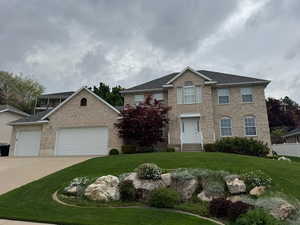 Colonial home with brick siding, fence, a garage, concrete driveway, and a front lawn