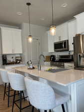 Kitchen featuring a sink, stainless steel appliances, a breakfast bar, backsplash, and white cabinets
