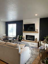 Living area featuring a textured ceiling, recessed lighting, a large fireplace, and wood finished floors