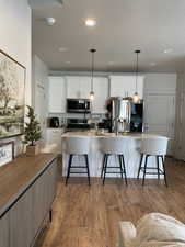 Kitchen with appliances with stainless steel finishes, a kitchen bar, an island with sink, and white cabinetry