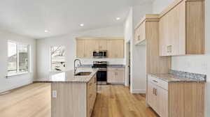 Kitchen featuring a sink, light wood-style flooring, light brown cabinetry, light stone countertops, and appliances with stainless steel finishes