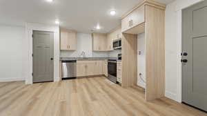 Kitchen with light wood-style flooring, a sink, light brown cabinets, baseboards, and appliances with stainless steel finishes