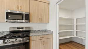 Kitchen with light brown cabinets, light wood-type flooring, modern cabinets, light stone countertops, and appliances with stainless steel finishes