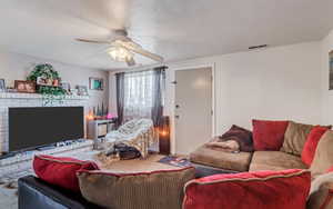 Carpeted living area with a fireplace, a ceiling fan, and visible vents