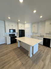 Kitchen featuring light wood finished floors, a center island, a sink, black appliances, and tasteful backsplash
