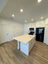 Kitchen with wood finished floors, black appliances, visible vents, white cabinets, and a kitchen island