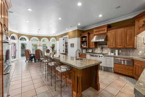 Kitchen featuring a sink, wall chimney exhaust hood, crown molding, a warming drawer, and light tile patterned flooring