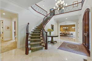 Entrance foyer featuring an inviting chandelier, crown molding, a towering ceiling, arched walkways, and stairs