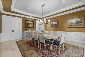 Dining area featuring an inviting chandelier, wainscoting, a raised ceiling, and ornamental molding
