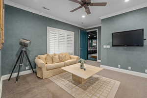 Carpeted living room featuring a ceiling fan, visible vents, baseboards, ornamental molding, and recessed lighting
