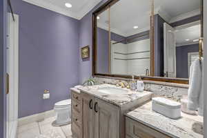 Bathroom featuring toilet, vanity, tile patterned floors, crown molding, and tiled shower