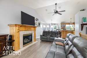 Living area with lofted ceiling, a tile fireplace, light wood-type flooring, and ceiling fan with notable chandelier