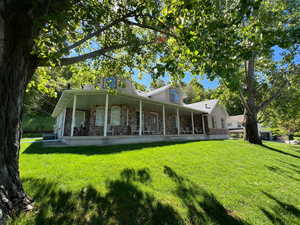 Rear view of property with a porch, a lawn, and stone siding