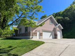View of front facade featuring stone siding, an attached garage, stucco siding, a front yard, and concrete driveway