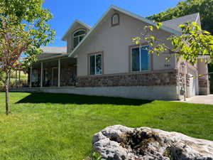 Rear view of property with stone siding, stucco siding, a yard, and a garage
