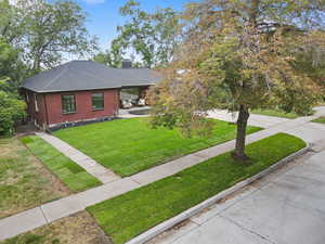View of front of house with brick siding, roof with shingles, a front yard, and a chimney