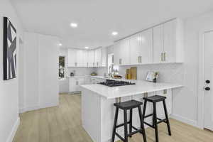 Kitchen with black gas cooktop, light wood finished floors, backsplash, and light countertops