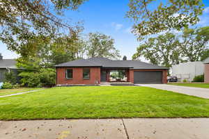 View of front of house featuring brick siding, a front yard, driveway, a chimney, and an attached garage