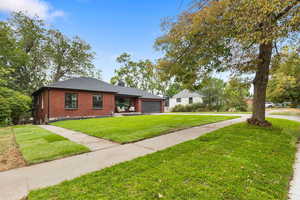 View of front of property featuring brick siding, a front yard, driveway, an attached garage, and roof with shingles
