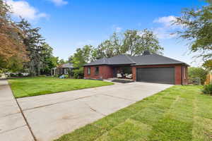 Single story home featuring brick siding, driveway, an attached garage, a front yard, and a chimney