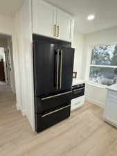 Kitchen view of white cabinets, black appliances, light wood finished floors, recessed lighting, and light stone counters