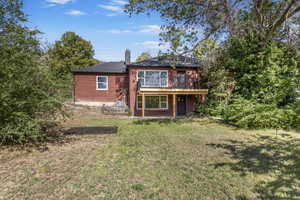 Rear view of house with brick siding, a chimney, and a deck