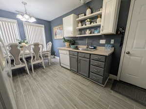 Kitchen with white dishwasher, a notable chandelier, wood tiled floor, a sink, and open shelves