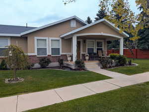 View of front of home featuring stucco siding, fence, a front lawn, a porch, and brick siding
