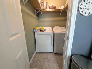 Clothes washing area with washing machine and dryer, baseboards, light tile patterned flooring, and laundry area