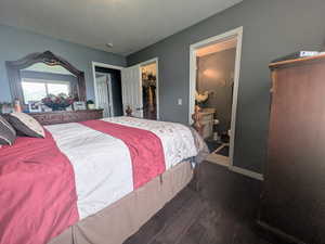 Bedroom with a closet, a walk in closet, baseboards, ensuite bath, and dark wood-style floors