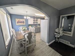Dining space featuring wood finish floors, visible vents, an inviting chandelier, arched walkways, and baseboards