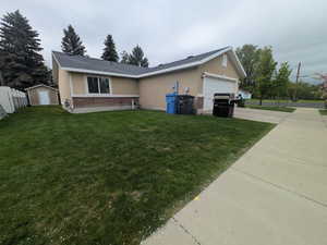 View of front of home with brick siding, an attached garage, concrete driveway, a front lawn, and a storage unit