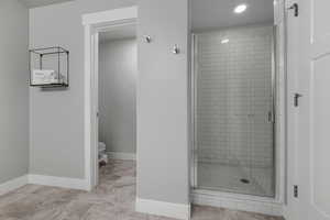 Bathroom featuring a stall shower, toilet, baseboards, and recessed lighting