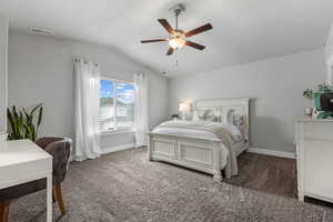 Carpeted bedroom with vaulted ceiling, ceiling fan, baseboards, and visible vents