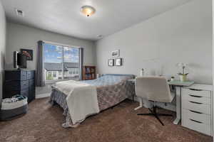 Bedroom with a textured ceiling, visible vents, baseboards, and dark carpet