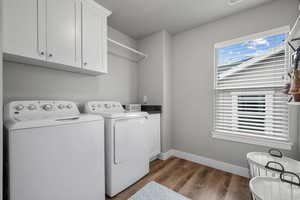 Clothes washing area with baseboards, separate washer and dryer, cabinet space, and wood finished floors