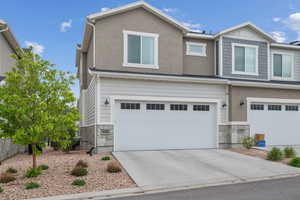 View of front of home featuring stone siding, a garage, and driveway