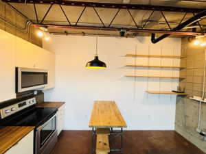 Kitchen with wooden counters, open shelves, stainless steel appliances, white cabinets, and concrete flooring