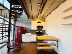 Kitchen with finished concrete flooring, a sink, white cabinetry, decorative backsplash, and stainless steel appliances