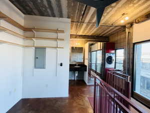 Kitchen with finished concrete flooring, stacked washer / drying machine, and electric panel