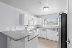 Kitchen featuring a textured ceiling, white appliances, a sink, white cabinetry, and a peninsula